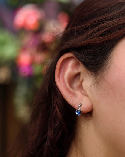 Modelo mostrando aros corazón colgante azul Swarovski de plata 925, diseño delicado Sylara.