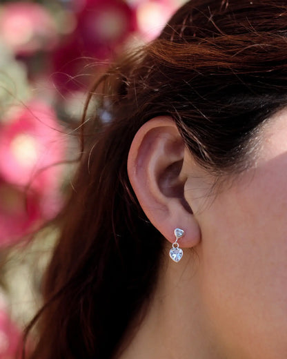 Modelo con aros con colgante de corazón blanco en plata 925, diseño elegante de Sylara.