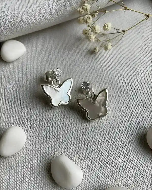 Detalle de los aros colgantes con mariposa blanca, joyería fina de Sylara.